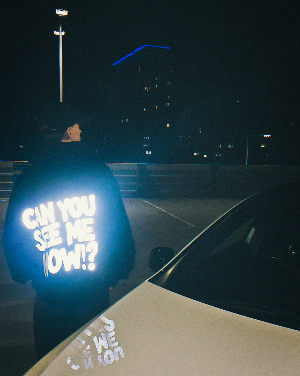 Person wearing a reflective hoodie with text in a dark setting
